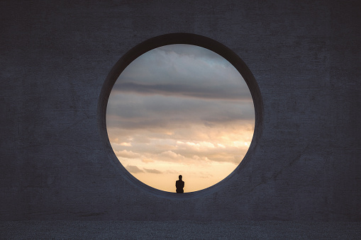 Lonely young woman looking through concrete window