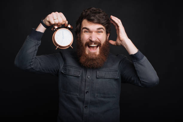 istock Shocked bearded man holding alarm clock and looking at camera 1196259574