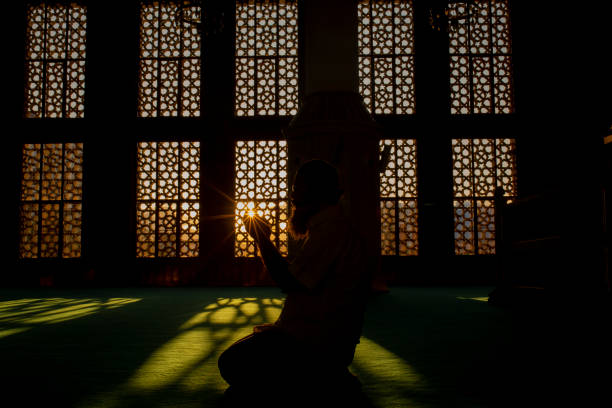 silhouette of a man worshiping in mosque stock photo