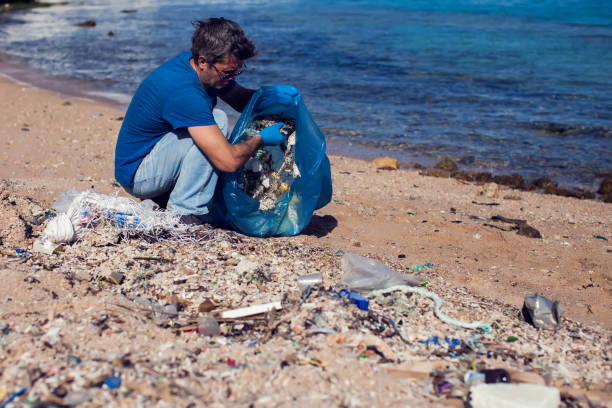 istock Man volunteer with big bag for trash collecting garbage on beach. Environmental pollution concept 1196275434