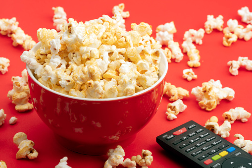 Fresh Popcorn in a red bowl and remote control over red background