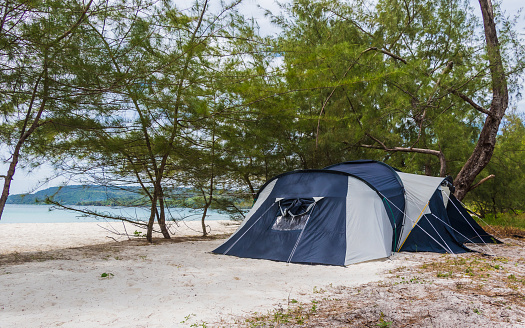 Big six person tent on the beach, blue grey, trees and ocean in the background