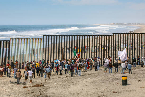 Dozens of migrants and workers on the sides of the US-Mexico border wall in Tijuana Beach Tijuana, Mexico, March 29 - Migrants and workers gather on both sides of the iron and steel wall that separates the border between Mexico and the United States in Playas de Tijuana. international border barrier stock pictures, royalty-free photos & images