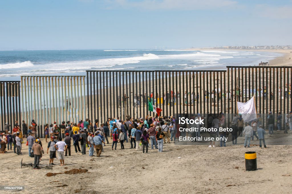 Migrants and workers meet along both sides of the US-Mexico border wall at Tijuana Beach in northern Mexico Tijuana, Mexico, March 29 - Migrants and workers gather on both sides of the iron and steel wall that separates the border between Mexico and the United States in Playas de Tijuana. Refugee Stock Photo