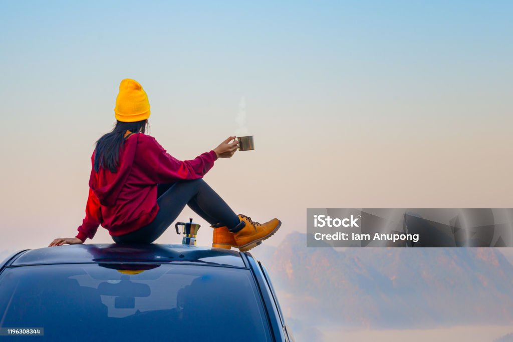 North 20 Woman traveller enjoy coffee time on her owns roof of the car with scenery view of the mountain and mist morning in background"n Car Stock Photo