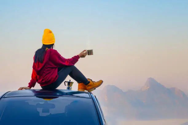 Woman traveller enjoy coffee time on her owns roof of the car with scenery view of the mountain and mist morning in background"n