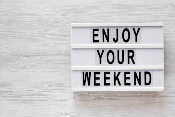istock 'Enjoy your weekend' words on a lightbox on a white wooden surface, top view. Overhead, from above, flat lay. Copy space. 1196317283