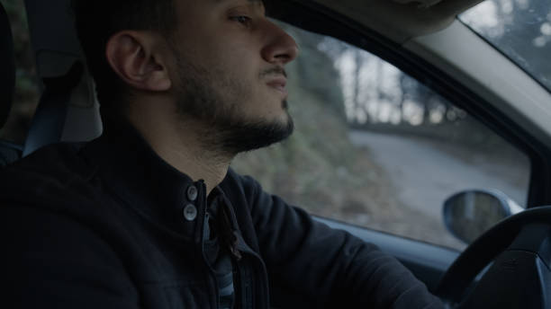 istock Young handsome bearded man in jacket smoking and driving in car, view from front passenger. Beautiful cityscape view out of the window 1196325471