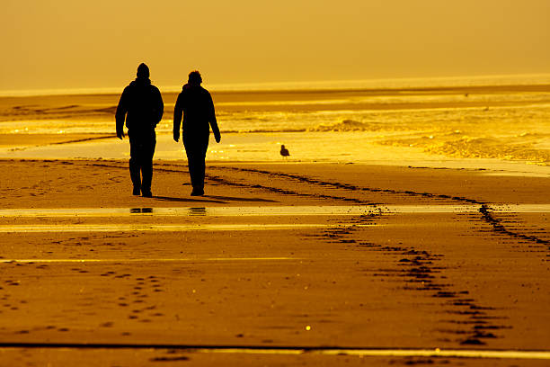 couple walking at a beach in the evening sun stock photo