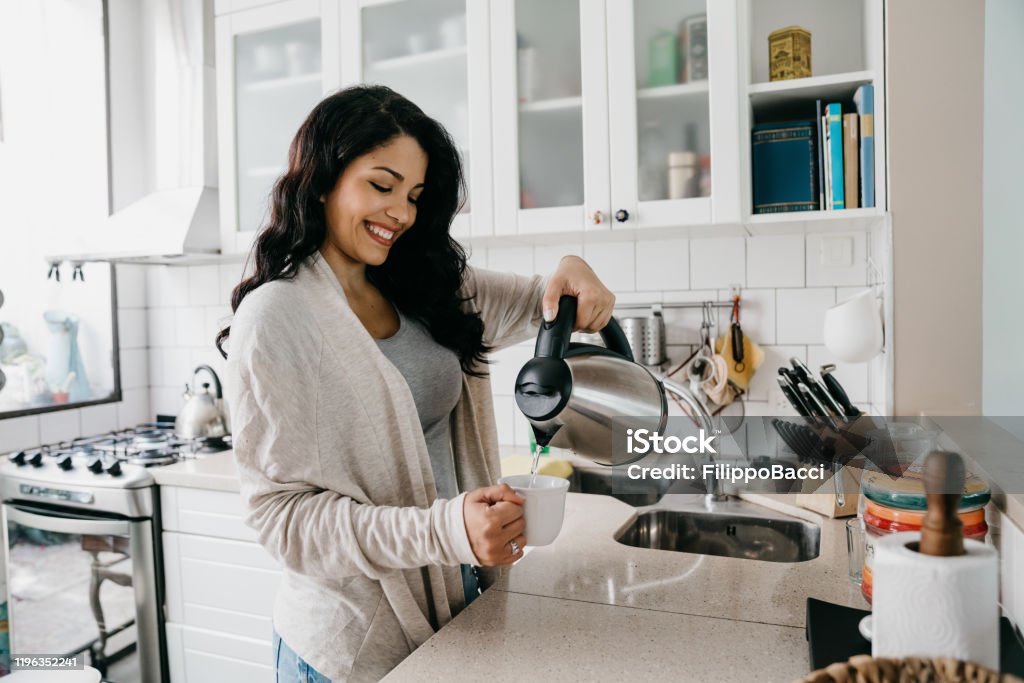 Young adult woman filling a cup of coffee Young adult woman filling a cup of coffee. She's smiling. Hispanic ethnicity. Kettle Stock Photo