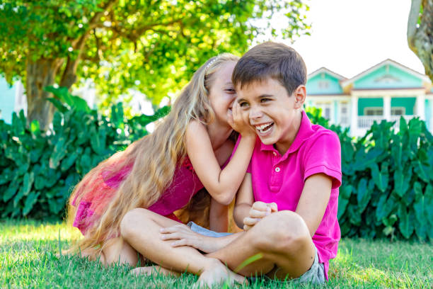 niña susurrando una broma en la oreja de un niño, niño se ríe, fondo de jardín de verano - whispering couple discussion smiling fotografías e imágenes de stock