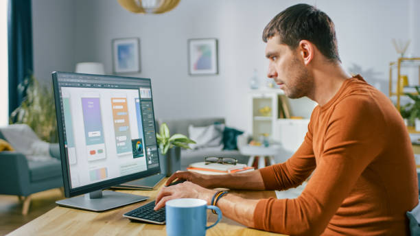 Handsome Software Engineer Works on a UX / UI Mobile App Template, Uses Personal Computer. Freelance Programmer Working At Home from Cozy Living Room. Handsome Software Engineer Works on a UX / UI Mobile App Template, Uses Personal Computer. Freelance Programmer Working At Home from Cozy Living Room. design professional stock pictures, royalty-free photos & images