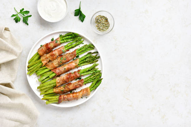 Bacon wrapped asparagus Bacon wrapped asparagus on white plate over light stone background with free text space. Top view, flat lay bacon wrapped stock pictures, royalty-free photos & images
