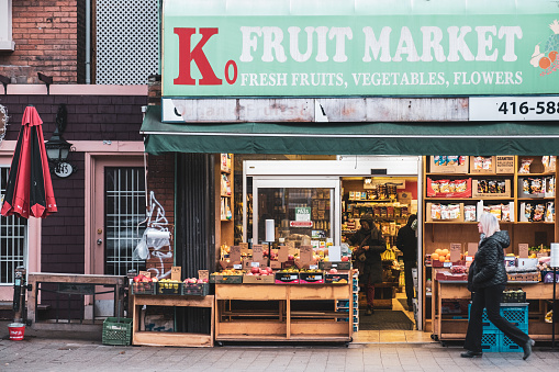 Toronto, ON 12/27/2019: Small fruit market store business with a pedestrian walking by in the eclectic strip of shops on Roncesvalles Ave.