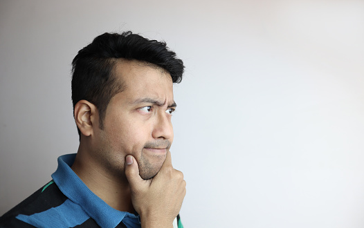 Portrait of thoughtful mature man in blue t-shirt looking up while standing against gray background.