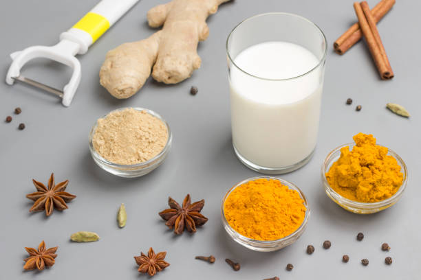 Milk in glass with ingredients for cooking Indian drink turmeric beverage Milk in glass with ingredients for cooking Indian drink turmeric beverage. Spices: cardamom, cinnamon sticks, star anise, turmeric, ginger, pepper, cloves on gray  background. ayurveda cardamom star anise spice stock pictures, royalty-free photos & images