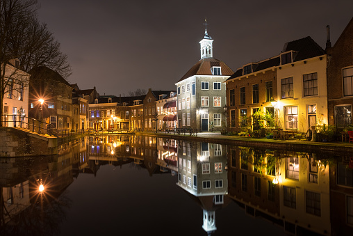 Classic dutch canal houses in the old town of Schiedam, Netherlands. Tall illuminated building with spire is known as 'The Porters' Guild House'.