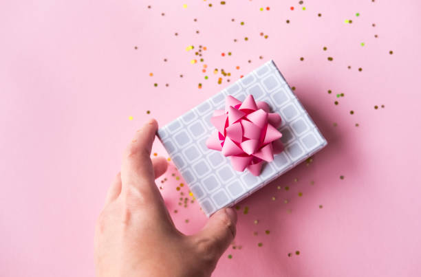 istock Silver gift box with pink bow in hand on pastel background in trendy flat lay composition with golden glitters. 1196388360