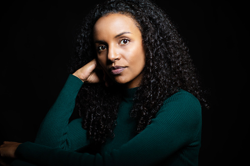 Portrait of an attractive mature african woman with curly hair staring at camera. Portrait of thoughtful woman in casuals with hand on chin against black background.