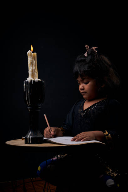 istock Cute little girl studying under candle light 1196393901