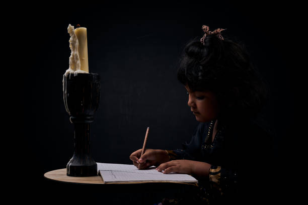 little girl escribiendo en candle light por la noche - slum living fotos fotografías e imágenes de stock