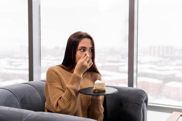 chica comiendo un pastel mientras se sienta en una silla frente a una ventana grande en un día de invierno - people winter urban scene chair fotografías e imágenes de stock