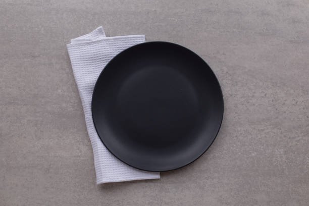 istock Dark plate with white napkin on grey stone table top view. Minimal Table setting. 1196406187