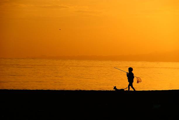 A little fisherman walk on the beach in sunset.