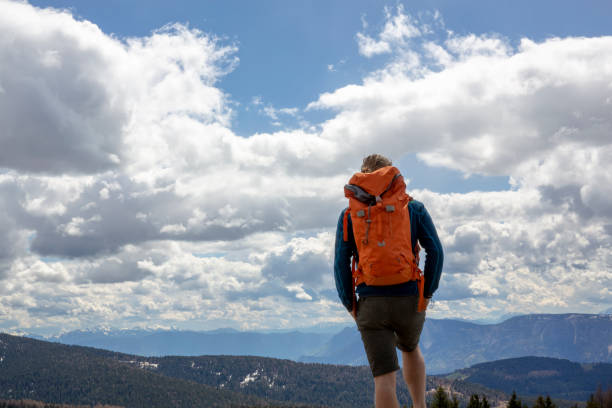 istock Young man with backpack looks across mountains and clouds 1196408609