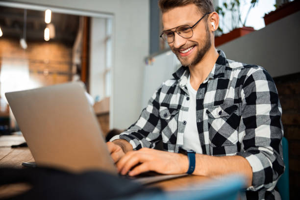 istock Happy young guy in glasses using laptop in cafe 1196409222