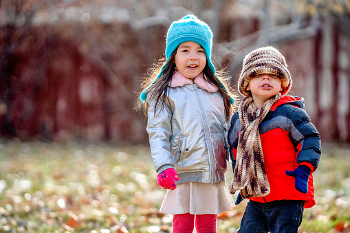 Mixed Race Boy and Girl Smiling and Playing in her Backyard Dressed up Warmly for Winter Fun