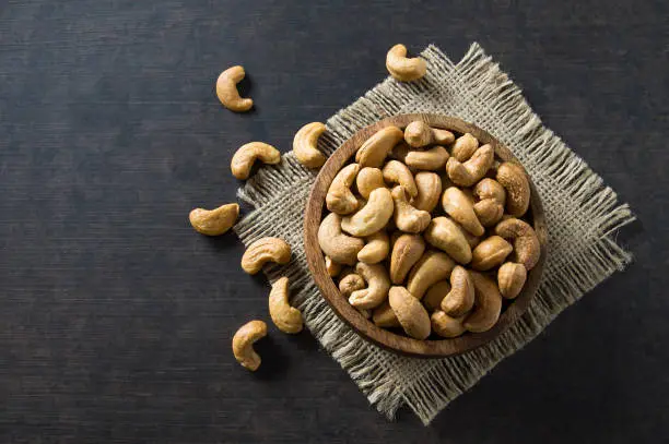 roasted salted raw cashew nuts in wooden bowl on rustic table, healthy vegetarian snack, Anacardium occidentale