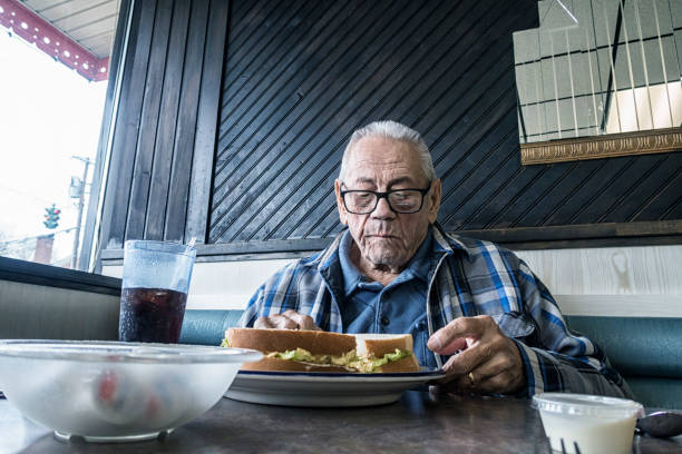 Elderly Man in Restaurant Chewing Egg Salad Sandwich