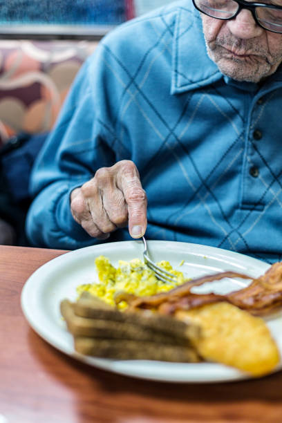 istock Elderly Arthritic Man Eating Scrambled Eggs Breakfast in Restaurant 1196423709