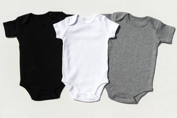 istock A set of three blank baby bodysuits on a cream textile background in harsh light - Black, white and grey baby grow set mockup - Styled stock photography 1196431455