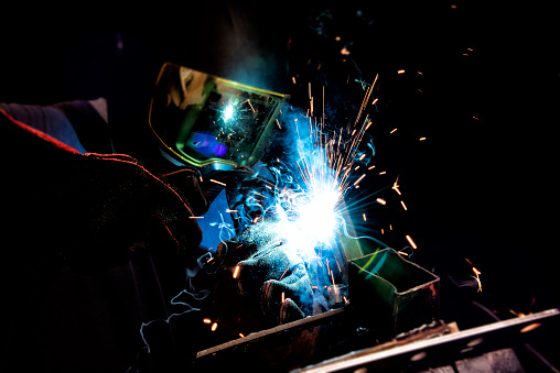 A male welder working in a shop welding steel for a manufacturing project.