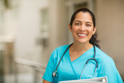 Smiling female healthcare professional looks at the camera while in hospital hallway. She is standing with her arms crossed.