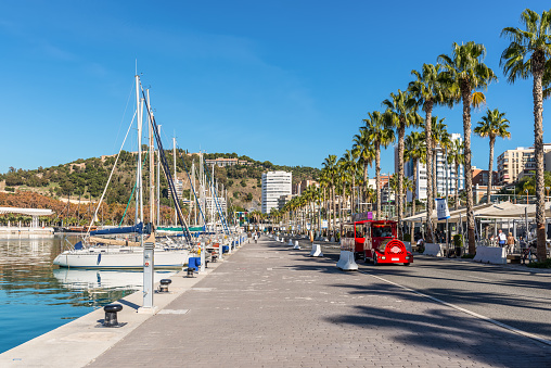 Malaga, Spain - December 4, 2018: Yachts and people at the Paseo del Muelle Uno (Pier One Walk), a beachfront shopping and leisure area in Malaga, Andalusia, Spain.