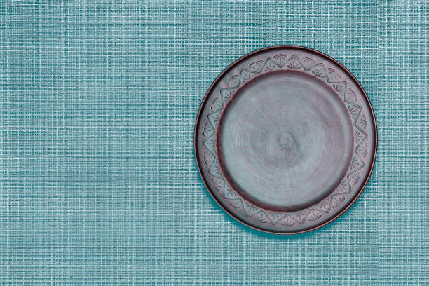 Brown ceramics dish (plate) on blue classic color bamboo mat. Flat lay.