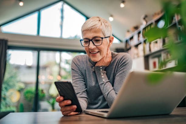 portret wesołego starszego bizneswoman za pomocą inteligentnego telefonu w domowym biurze, z bliska. - telecommuting technology equipment one person zdjęcia i obrazy z banku zdjęć