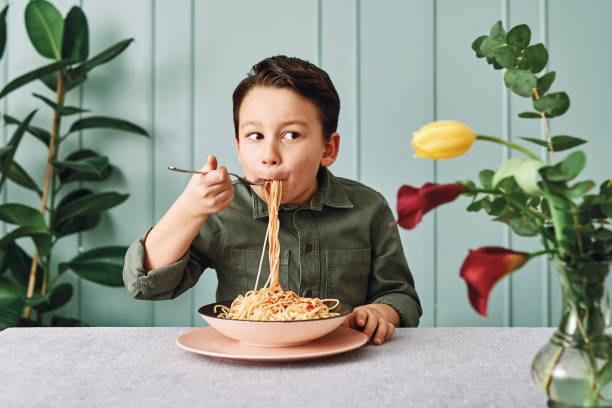 6-7 jahre alt süßes kind essen spaghetti. er ist glücklich. - 6 7 years stock-fotos und bilder