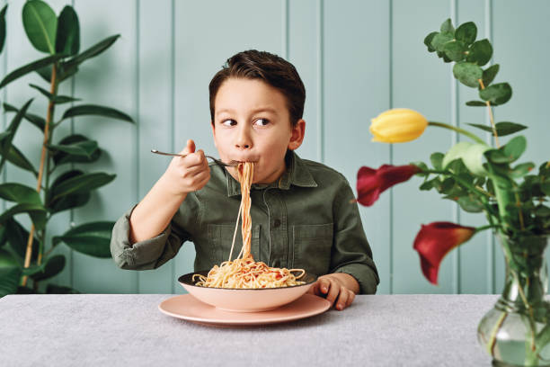 6-7 ans enfant mignon mangeant des spaghettis. il est heureux. - child eating pasta spaghetti photos et images de collection