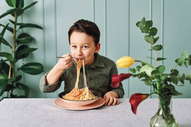 bambino carino di 6-7 anni che mangia spaghetti. è felice. - 6 7 years foto e immagini stock