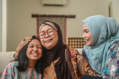 A portrait of happy Asian Muslim young girl with mother and grandmother sitting at home during Hari Raya celebration