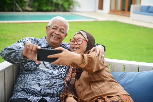 An happy smiling Indonesian senior couple sitting on wooden bench at home An happy smiling Indonesian senior couple sitting on wooden bench at home malay couple stock pictures, royalty-free photos & images
