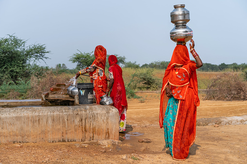 Pushkar, India - November 04, 2019: Kalbeliya gypsy women in colorful clothes collect and carry on their head drinking water at public tap in desert on November 04, 2019 in Pushkar, Rajasthan, India.