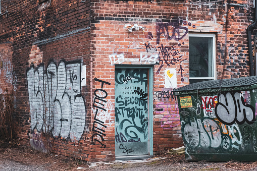 Toronto, ON. 12/27/2019: Winter scene of dilapidated entrance to old brick building off Queen St. Graffiti covers entire back area of building including dumpster.