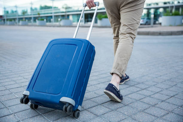 Stylish man walking to airport with blue suitcase. Businessman traveling.