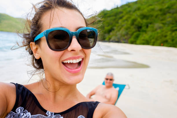 Beach Selfie Beautiful young multicultural woman taking a selfie at the beach with her father photobombing in the background. photo bomb stock pictures, royalty-free photos & images