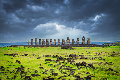 Famous Ahu Tongariki, all fifteen standing Moai Statues side by side illuminated by the sun in a row under dramatic stormy cloudscape. Easter Island, Isla de Pascua, Polynesia, Chile, Oceania
